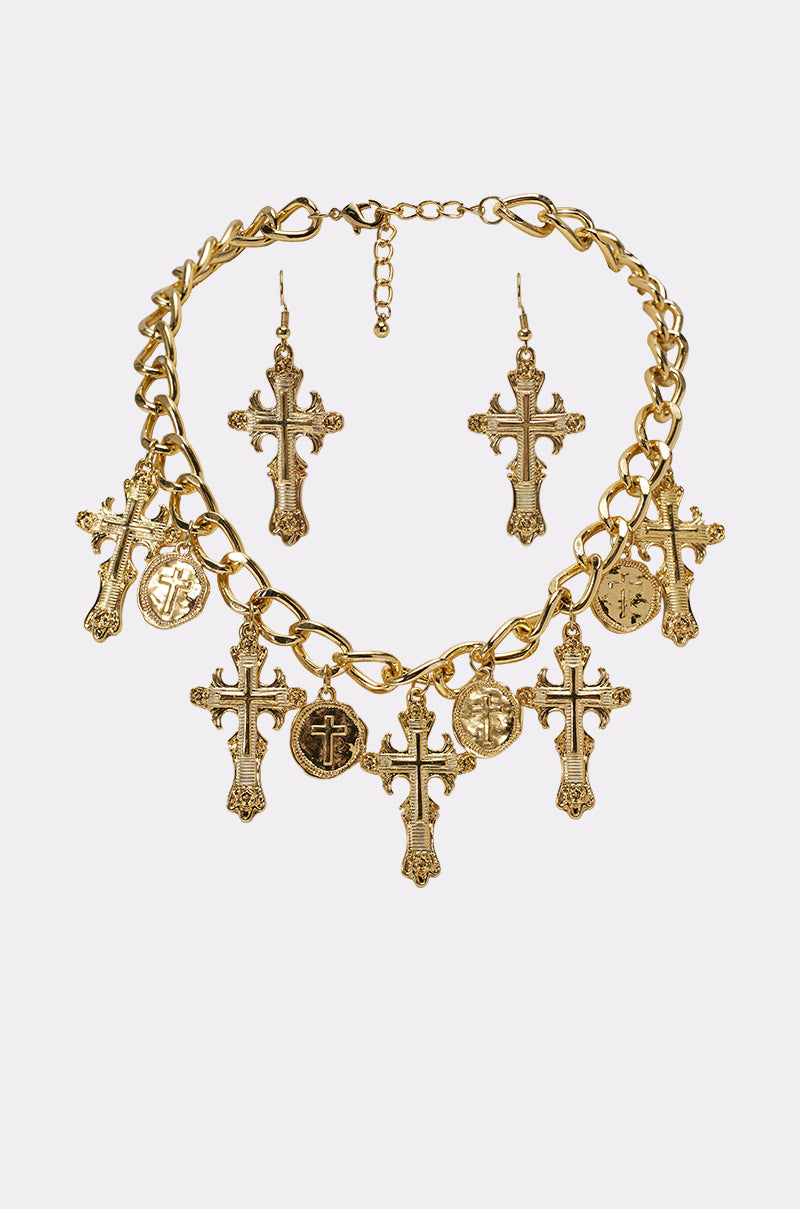 The CHARMED LIFE NECKLACE, a gold cross necklace with coin pendants, is paired with matching cross earrings and displayed on a white background. 2