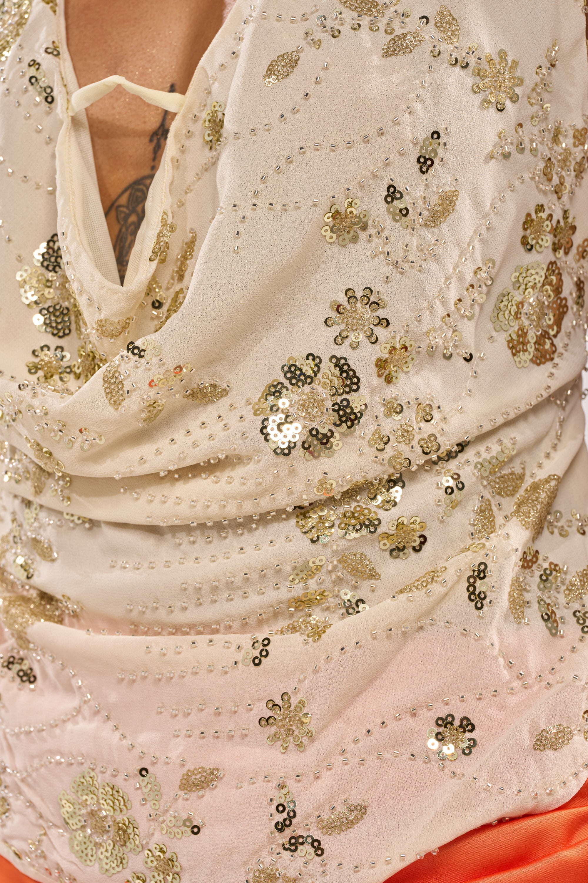 Close-up of the JULIE Baby Yellow Halter Top with sequins and beadwork in floral patterns—ideal for festival looks—worn by a person with a tattoo partially visible above the neckline. 7