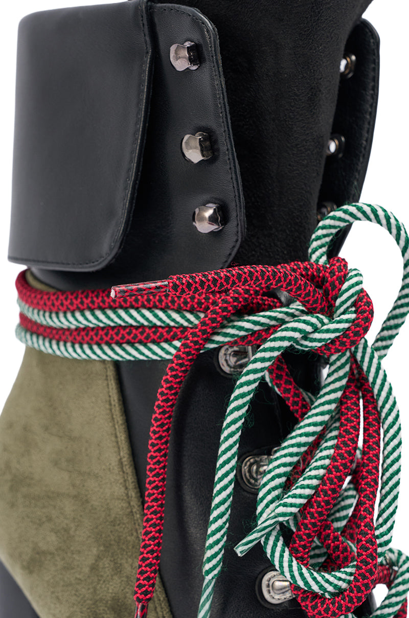 A close-up of the AKIRA GOLD MUFFLER GREENMULTI CHUNKY HEEL BOOTIE, featuring olive green faux suede, a black flap with metal eyelets, thick red-and-green striped laces in a bow, and a rugged platform lug sole.