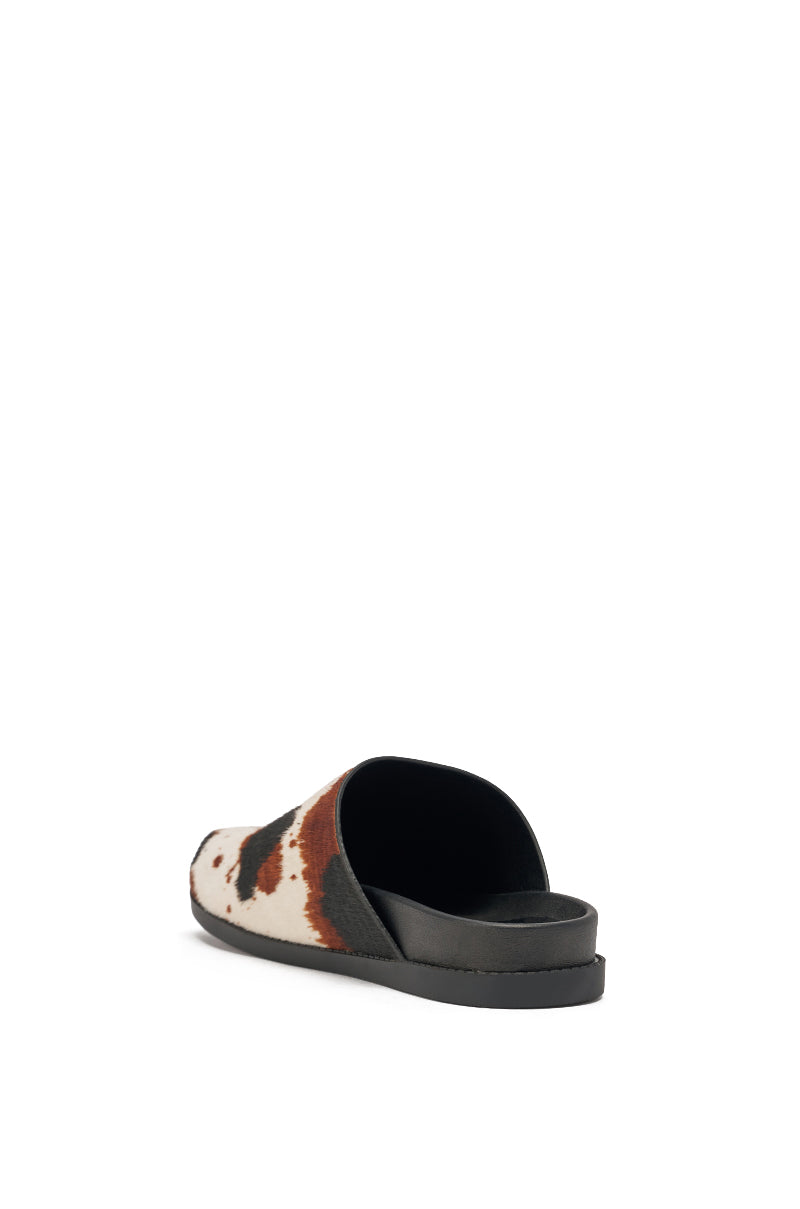 The AZALEA WANG MUKEY COW PRINT CALF HAIR FLAT is a single backless slip-on mule with a black sole and a brown, black, and white cow print genuine calf hair upper, shown from a rear side angle against a white background. 6