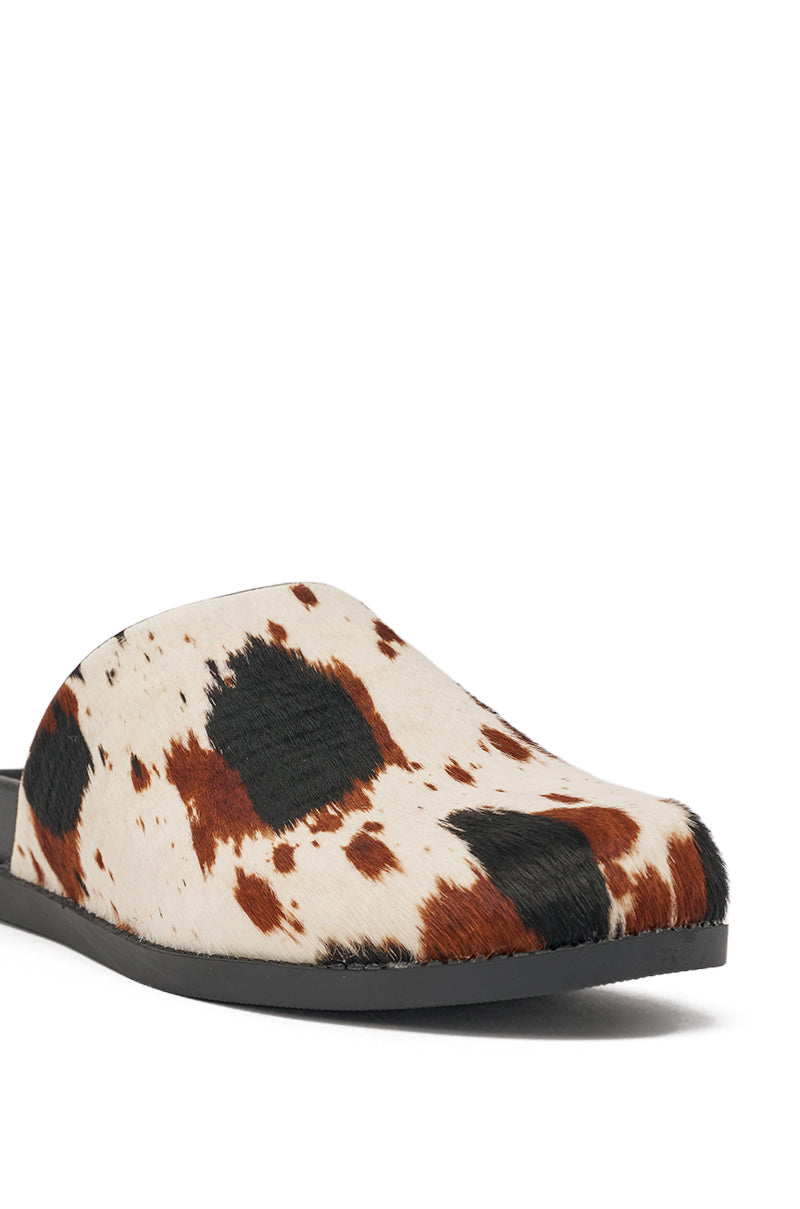 A close-up of the AZALEA WANG MUKEY COW PRINT CALF HAIR FLAT slip-on mules, showcasing genuine calf hair with black and brown cow-print spots and a flat black sole. 7