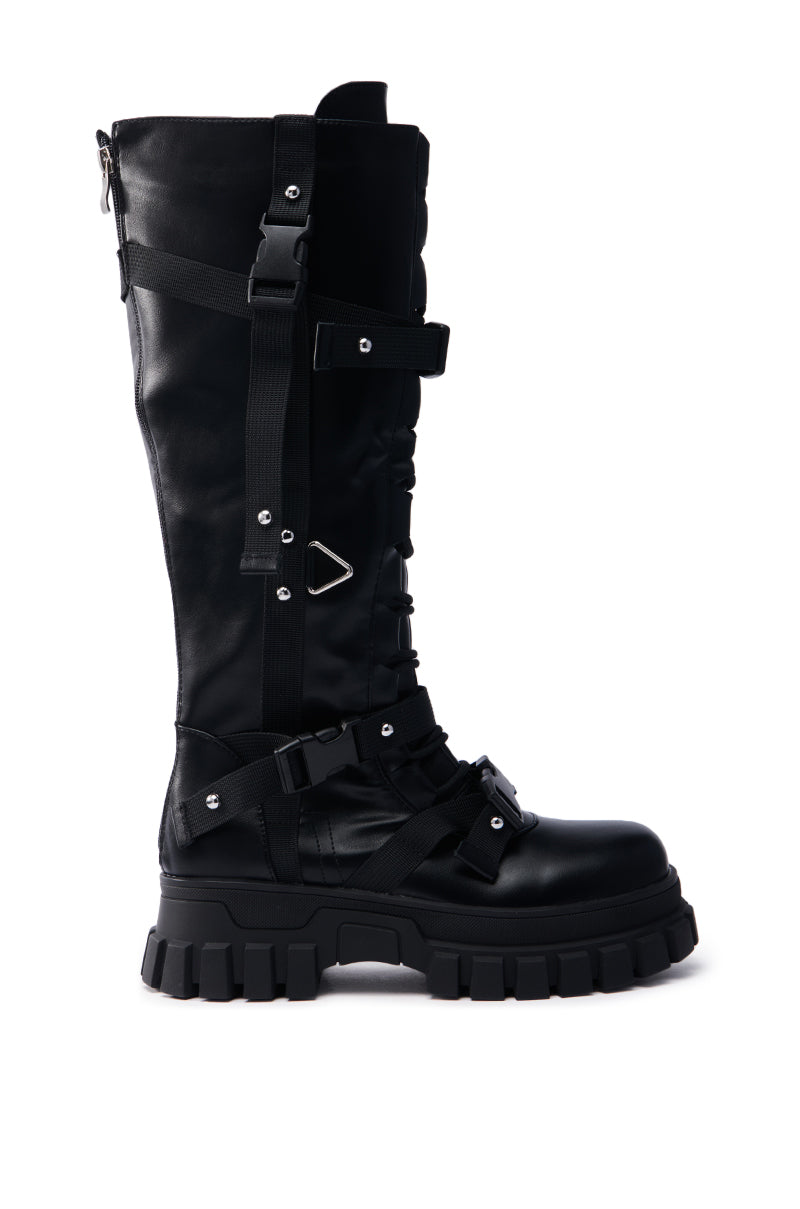 The AZALEA WANG MYRON BLACK BOOT is a black faux leather knee-high with chunky soles, multiple straps, laces, metal hardware details, and a side zipper. These punk princess boots offer a rugged design ideal for an edgy fashion statement.