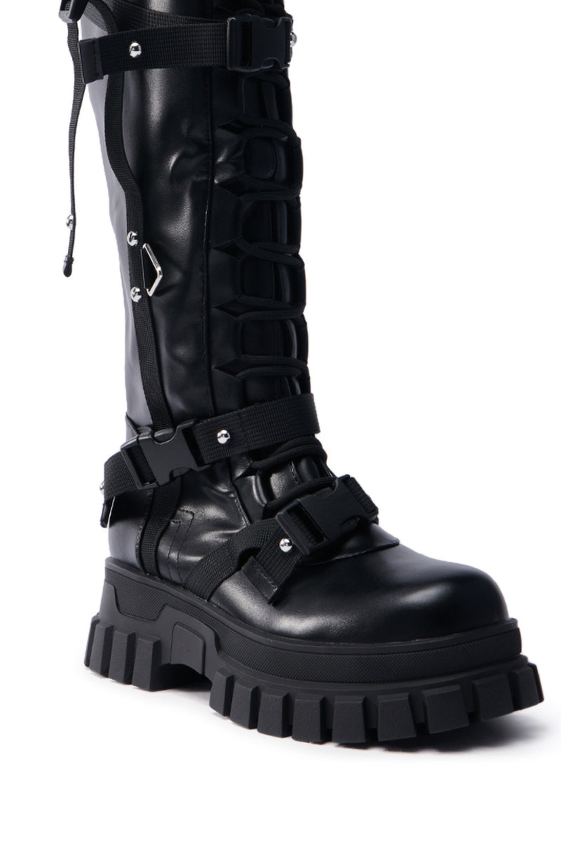 The AZALEA WANG MYRON BLACK BOOT is a pair of knee-high black faux leather boots featuring chunky platform soles, silver buckles, straps, laces, and rugged combat-inspired hardware details.