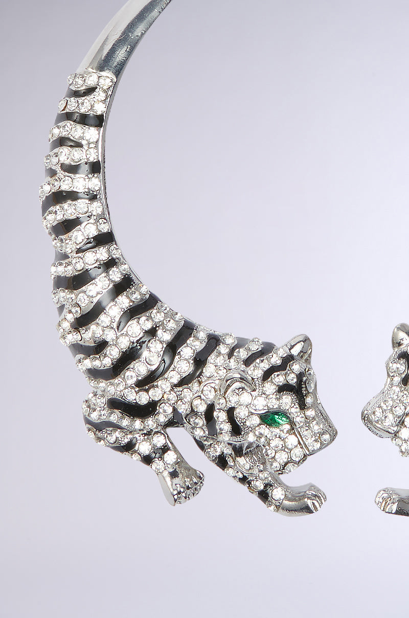 The ON THE PROWL CHOKER is a silver brooch showcasing a tiger with sparkling rhinestones, vivid green eyes, and striking stripes artfully curved into a semi-circle against a gray background. 3