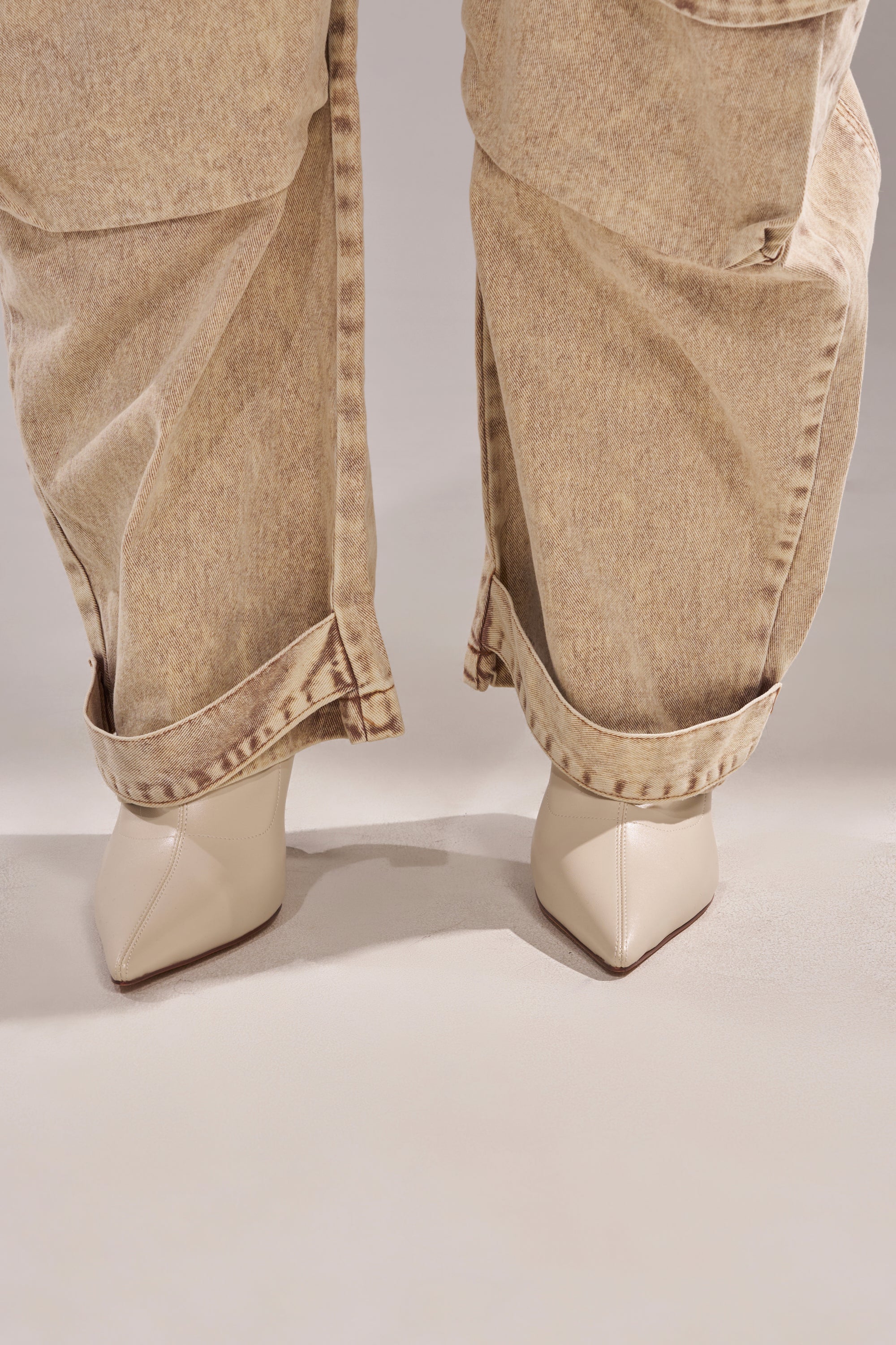 A close-up of a person wearing the JESSICA DENIM CARGO JUMPSUIT and cream pointed-toe heels, standing on a light surface. 6