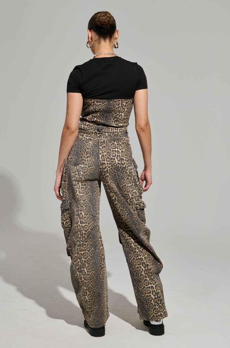 With their back to the camera, an individual exudes fierce energy in the FIERCE ENERGY ONLY LEOPARD JUMPSUIT. Their short hair and the jumpsuit's wide leg silhouette harmonize perfectly against the plain gray backdrop.
