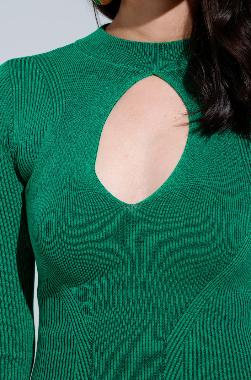 A person wearing the ABOUT YOU Midi Dress in green, showcasing a distinctive oval cutout at the chest. This bodycon fit features long sleeves and beautifully hugs the silhouette. The individual's long, dark hair cascades over one shoulder, adding an elegant touch to the ensemble.