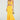 A woman holds a small woven bag and wears the "LOOKING FOR FUN KNIT MAXI DRESS IN YELLOW," featuring a cutout and flared asymmetrical hem. She pairs it with platform sandals against a plain, light-colored backdrop.