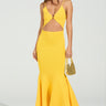 A woman holds a small woven bag and wears the "LOOKING FOR FUN KNIT MAXI DRESS IN YELLOW," featuring a cutout and flared asymmetrical hem. She pairs it with platform sandals against a plain, light-colored backdrop.
