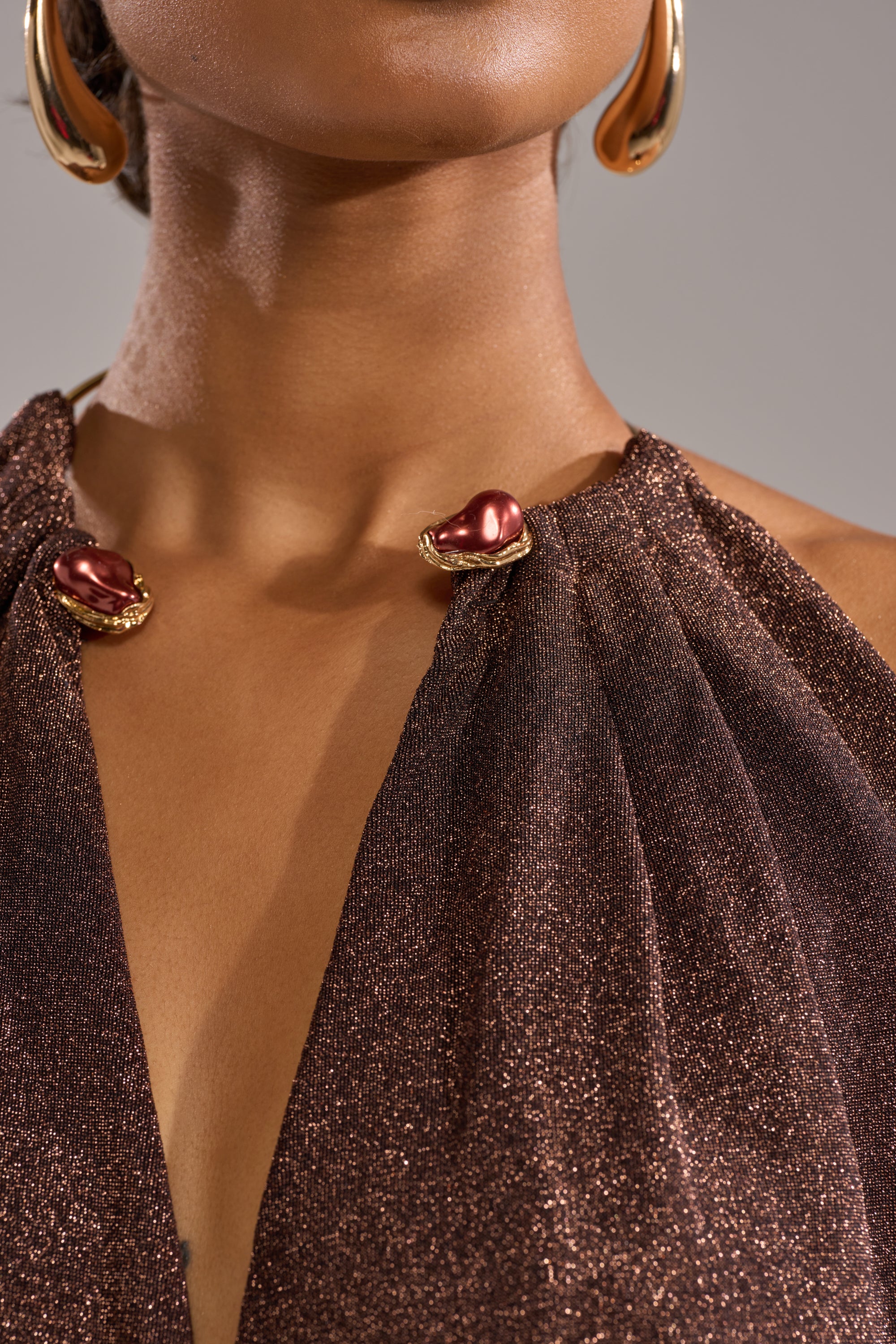 A close-up of someone wearing the VEGAS NIGHTS MINI DRESS, showcasing its sleek fit and metallic red and gold clasps at the neckline, paired with large gold hoop earrings against a neutral background.