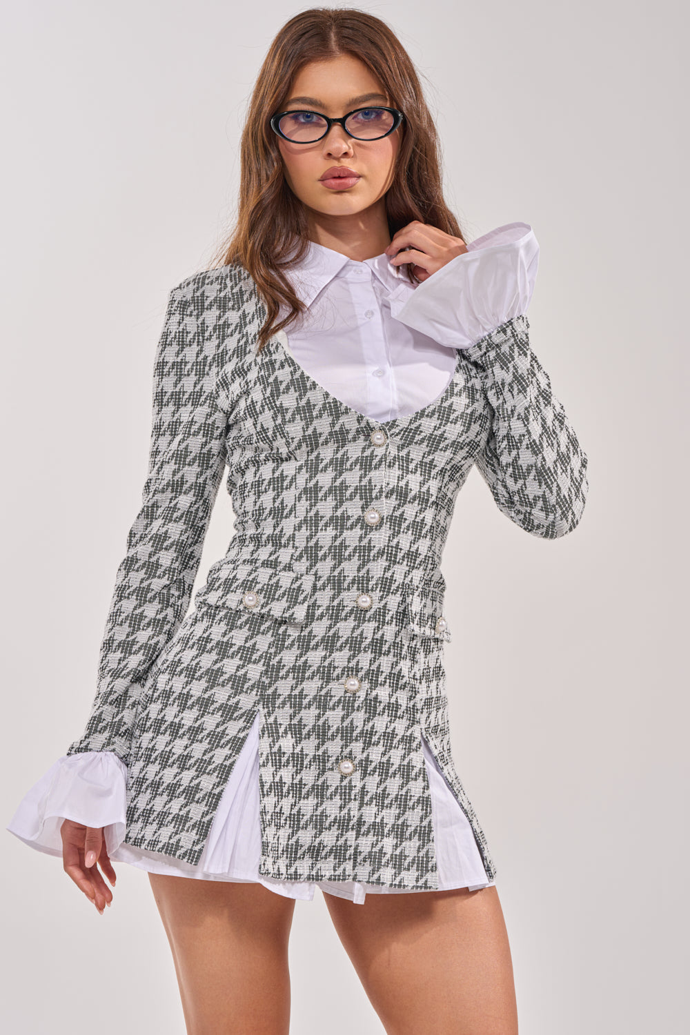 A woman with long brown hair and glasses models the TALIA TWEED LONG SLEEVE COLLARED DRESS, featuring a plaid vest and skirt set with flared cuffs, against a plain light background. 0