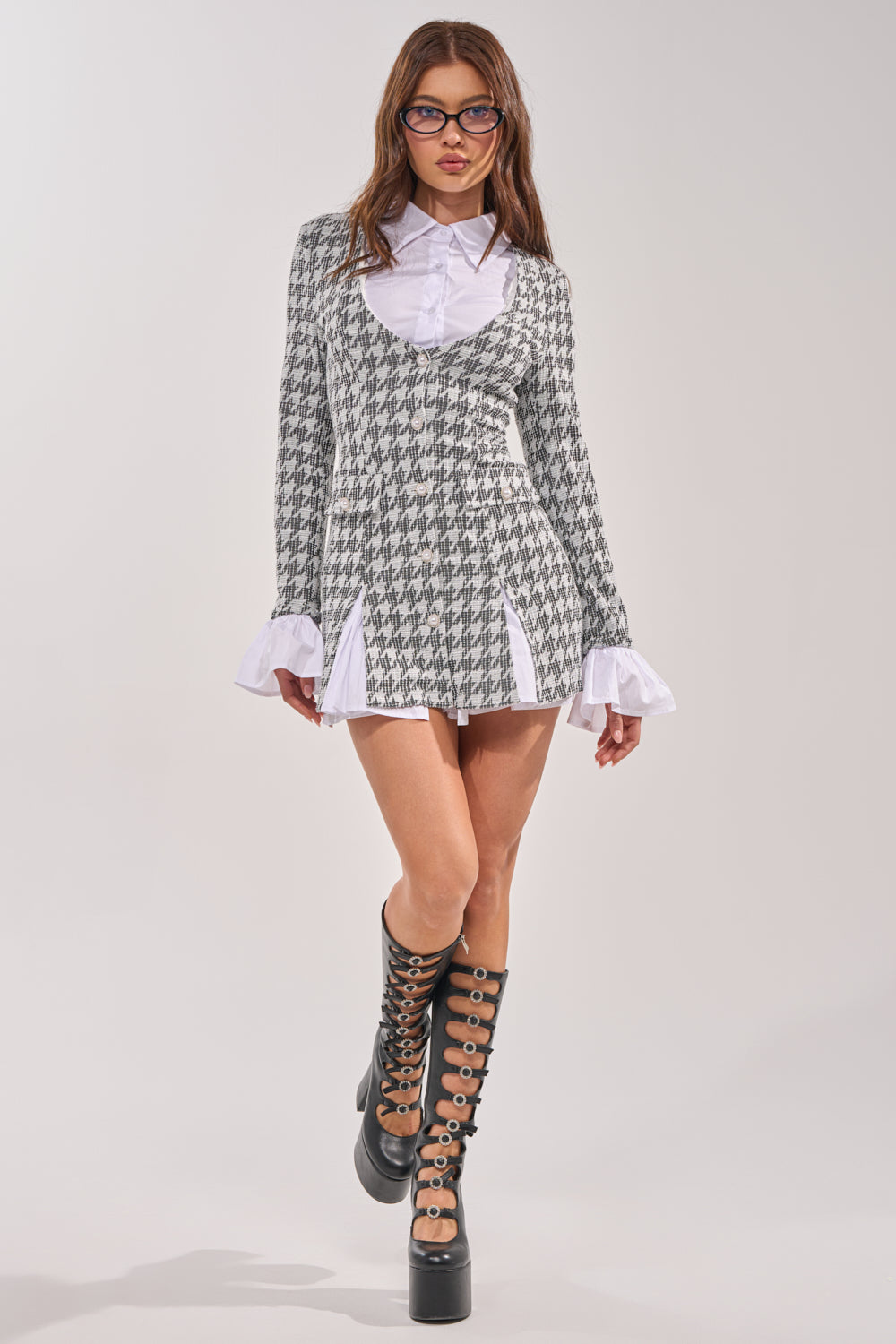 A woman in glasses wears the TALIA TWEED LONG SLEEVE COLLARED DRESS over a white ruffled-cuff shirt, paired with knee-high black platform boots with circular cutouts, standing against a plain light background. 5