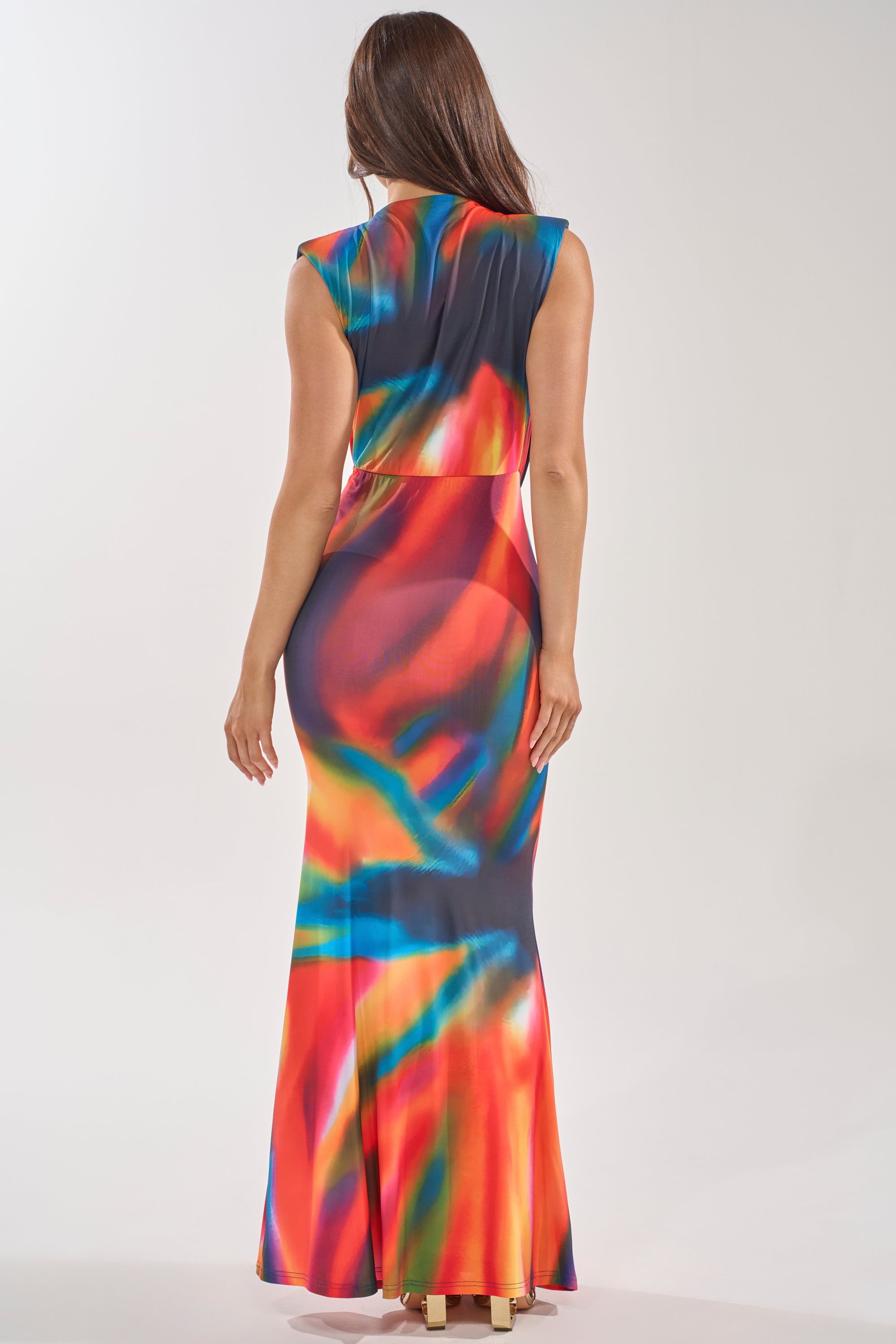 A woman faces away, wearing the COLOR ME IMPRESSED MAXI DRESS—a sleeveless, form-fitting maxi with a vibrant multicolor abstract watercolor print—set against a plain light background. 4