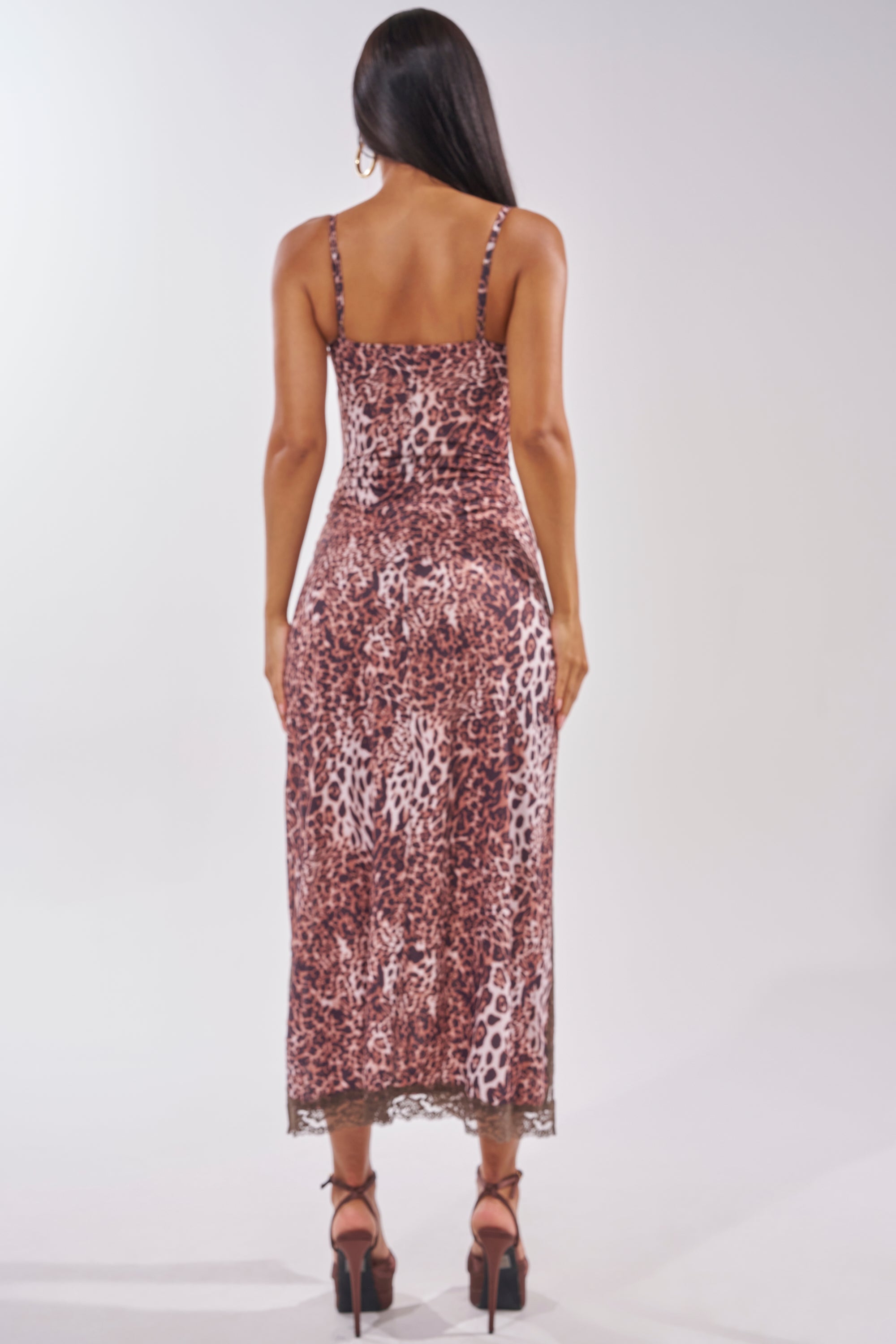 A woman with long dark hair faces away, wearing the SWEET DREAMS LACE MAXI DRESS IN CHEETAH—a striking lace maxi in cheetah print—paired with strappy heels against a simple light background, perfect for date night. 5