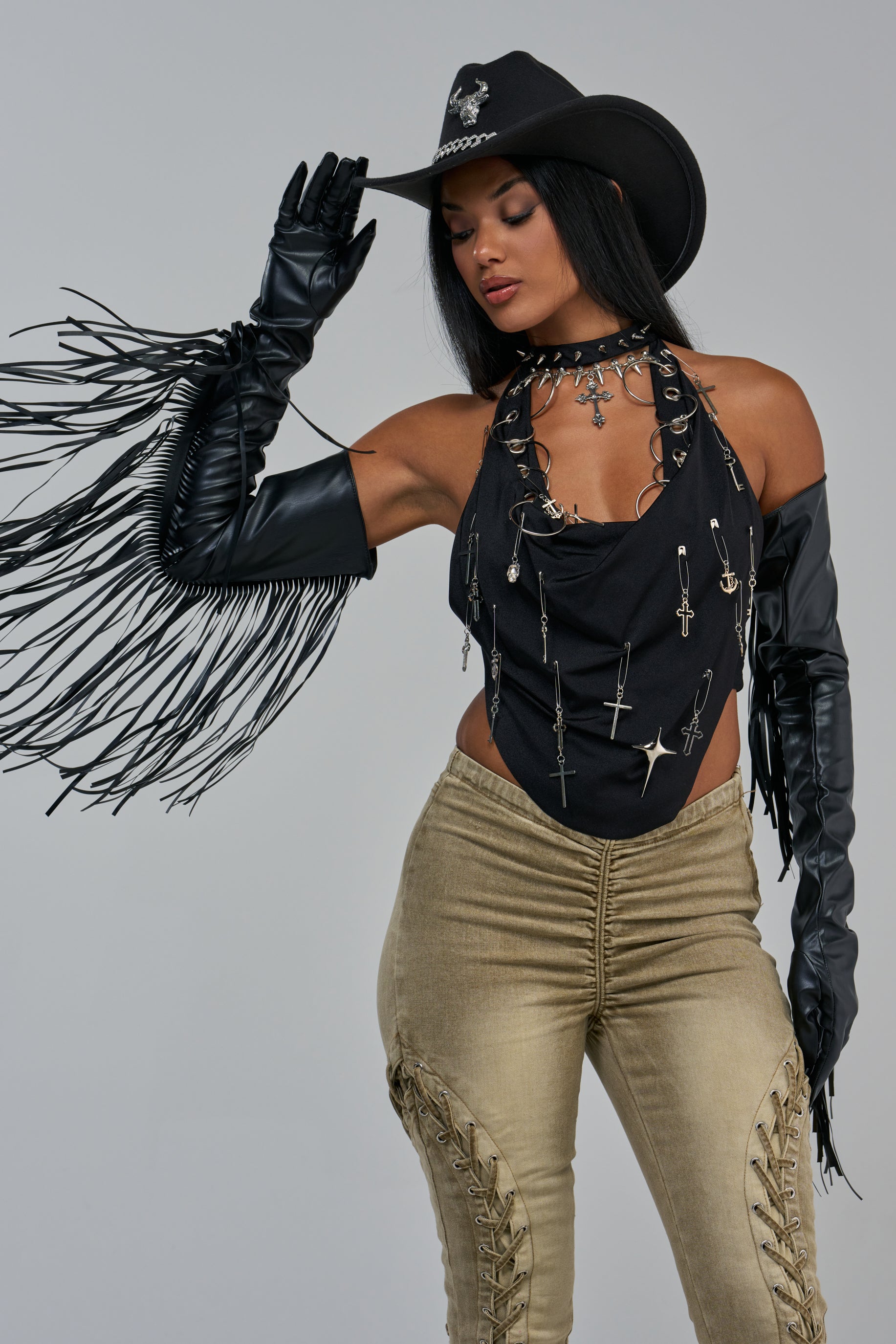 A person wearing a black cowboy hat, a halter top adorned with silver charms, and black FRINGE APPEAL LONG GLOVES.