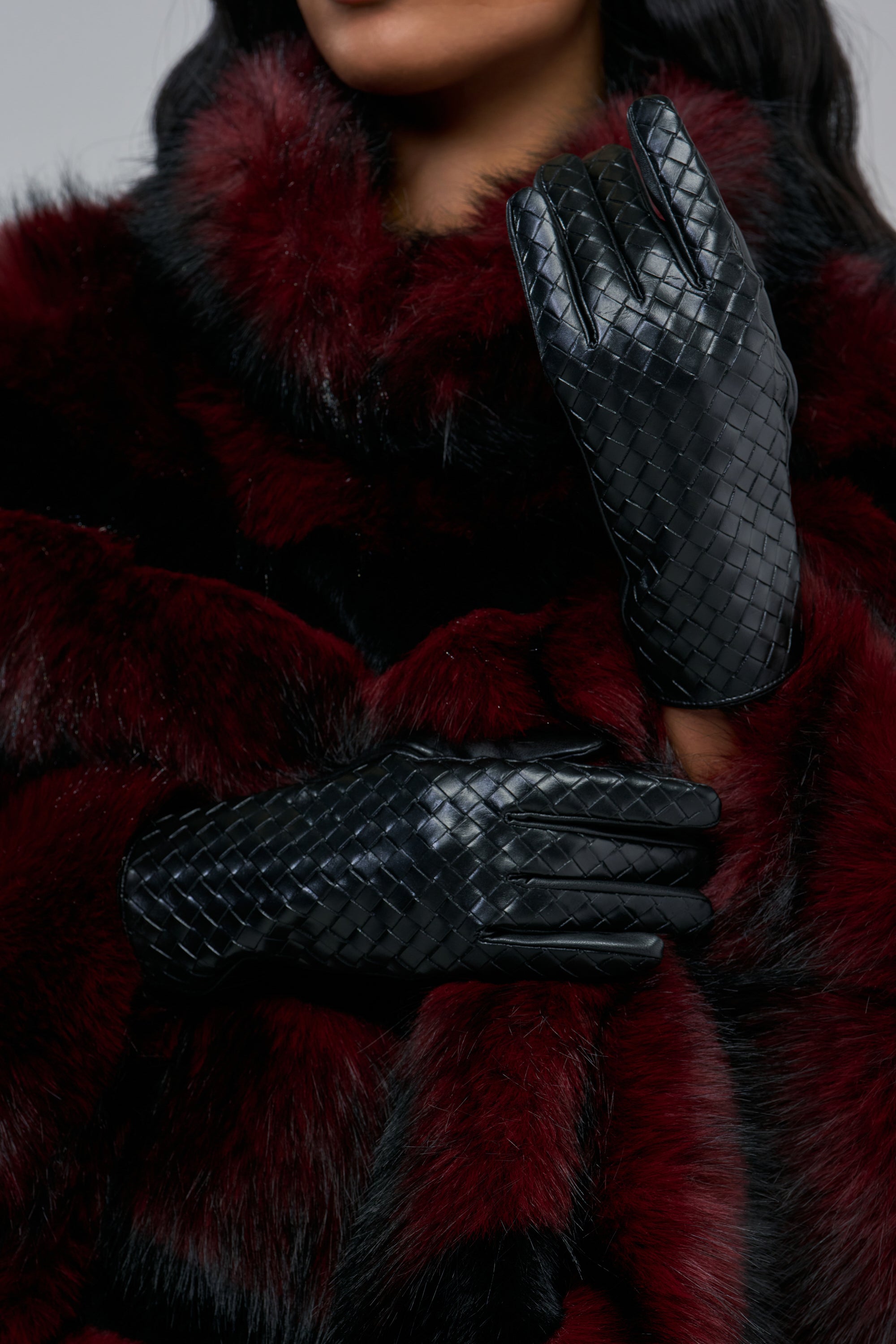 A person wearing black woven faux leather DEVILS IN THE DETAILS SHORT GLOVES and a dark red faux fur coat.