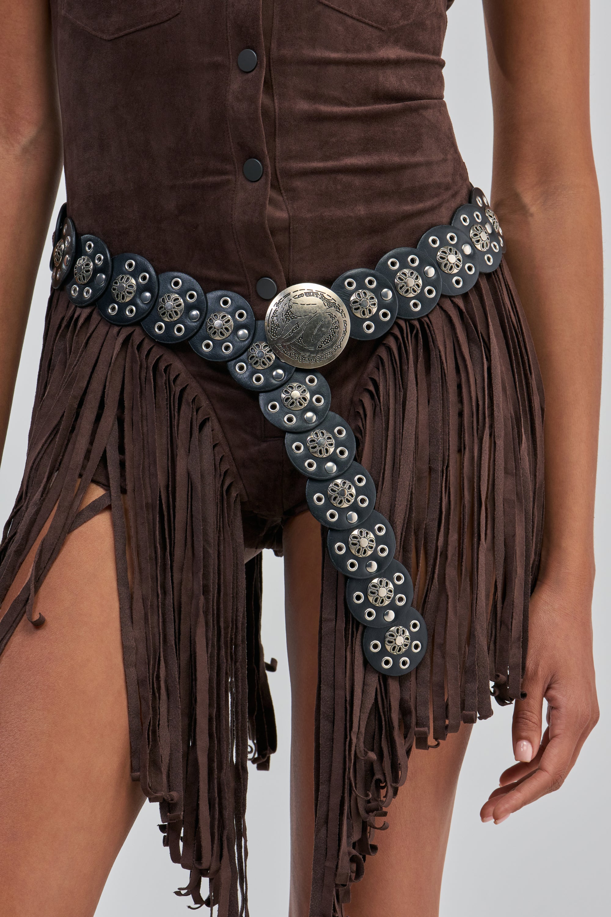 A person wearing a brown suede outfit with fringe detailing, accessorized with the SAVE A HORSE BELT—a western-style belt featuring silver conchos and a large round buckle.