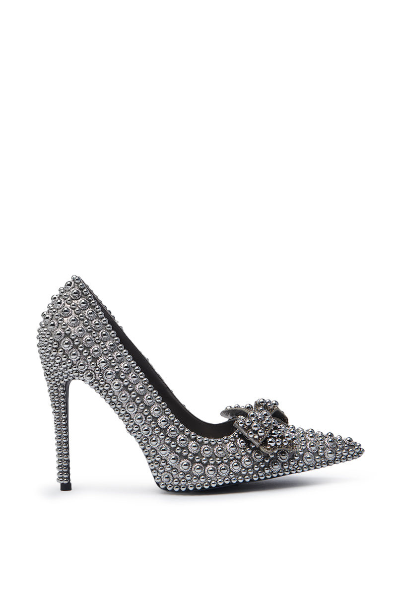 The AZALEA WANG HEMITATE STONE EMBELLISHED PUMP is a faux leather stiletto with silver studs, rhinestones, a pointed toe, and a jeweled bow accent on the front.
