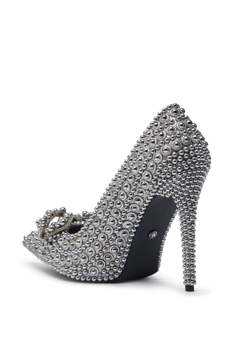The AZALEA WANG HEMITATE STONE EMBELLISHED PUMP is a faux leather stiletto heel with silver beads, rhinestones, a peep toe, and a decorative buckle, displayed from the rear side on a white background.