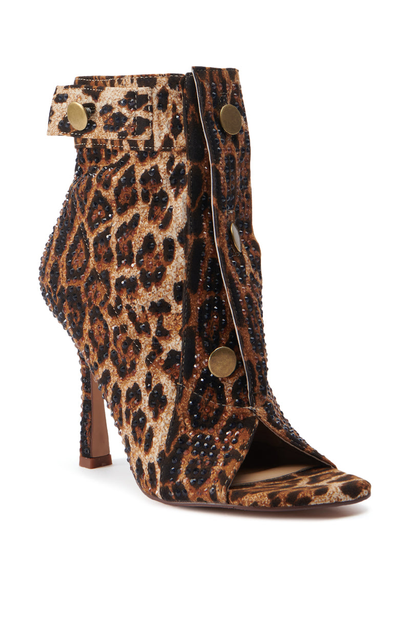 The AZALEA WANG NAILY CHEETAH BUTTON UP BOOTIE is a high-heeled ankle boot with a cheetah print and peep-toe design, featuring large gold buttons along the front and a decorative strap across the top. This stiletto heel bootie also includes scattered stud embellishments for added texture and sparkle, along with a comfort cushion insole for all-day wear. 3