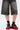 A person in faded black knee-length denim shorts, black socks, and the AZALEA WANG NAMIDA BURGUNDY SNEAKER with a platform rubber outsole stands against a plain white background, emphasizing streetwear appeal.