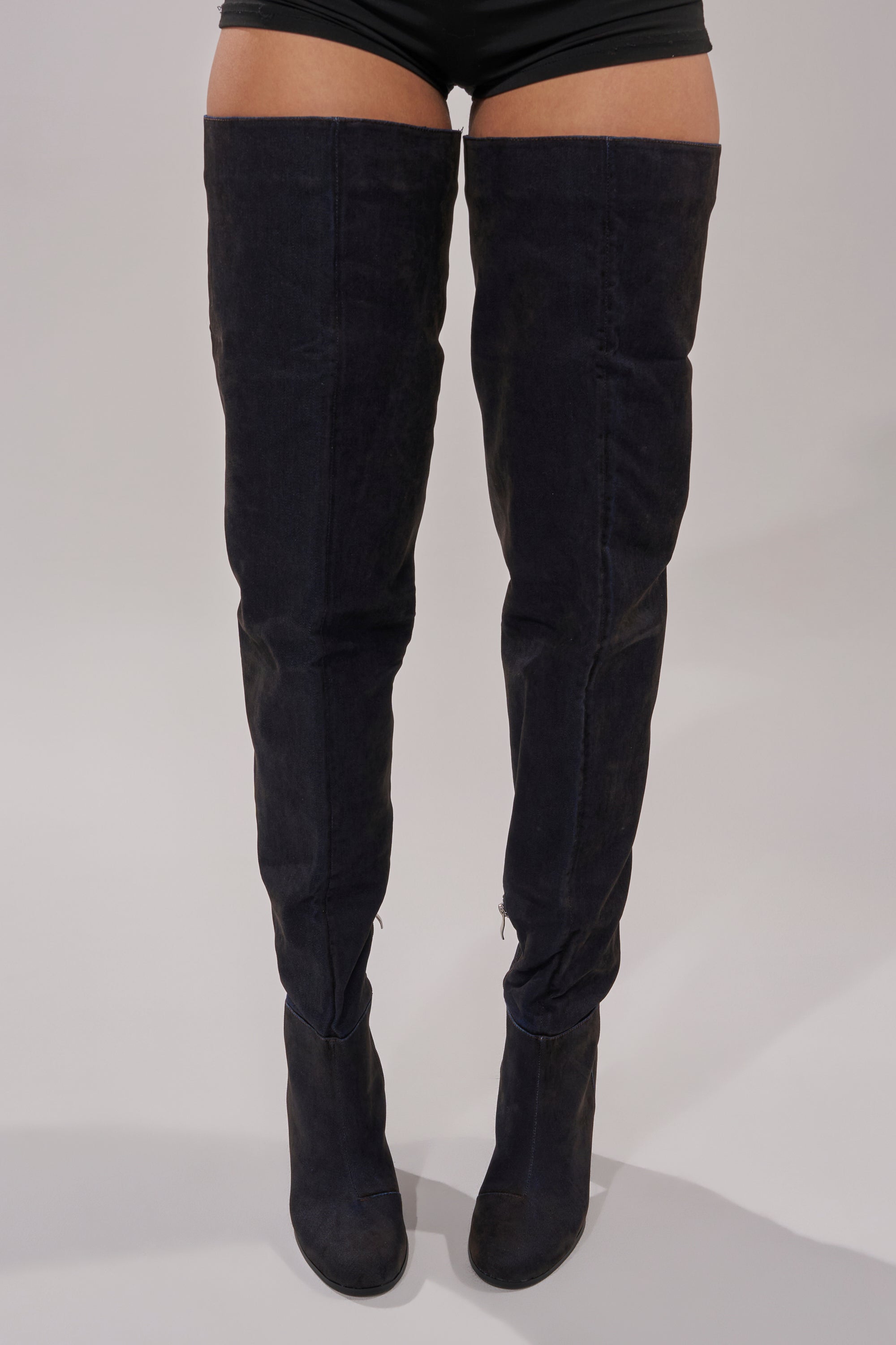 Only the legs and lower torso are visible as a person wearing high-waisted black shorts and AZALEA WANG NANETTE BLACK DENIM SLOUCHY BLACK ROUND TOE CHUNKY BOOTS stands against a plain light gray background.