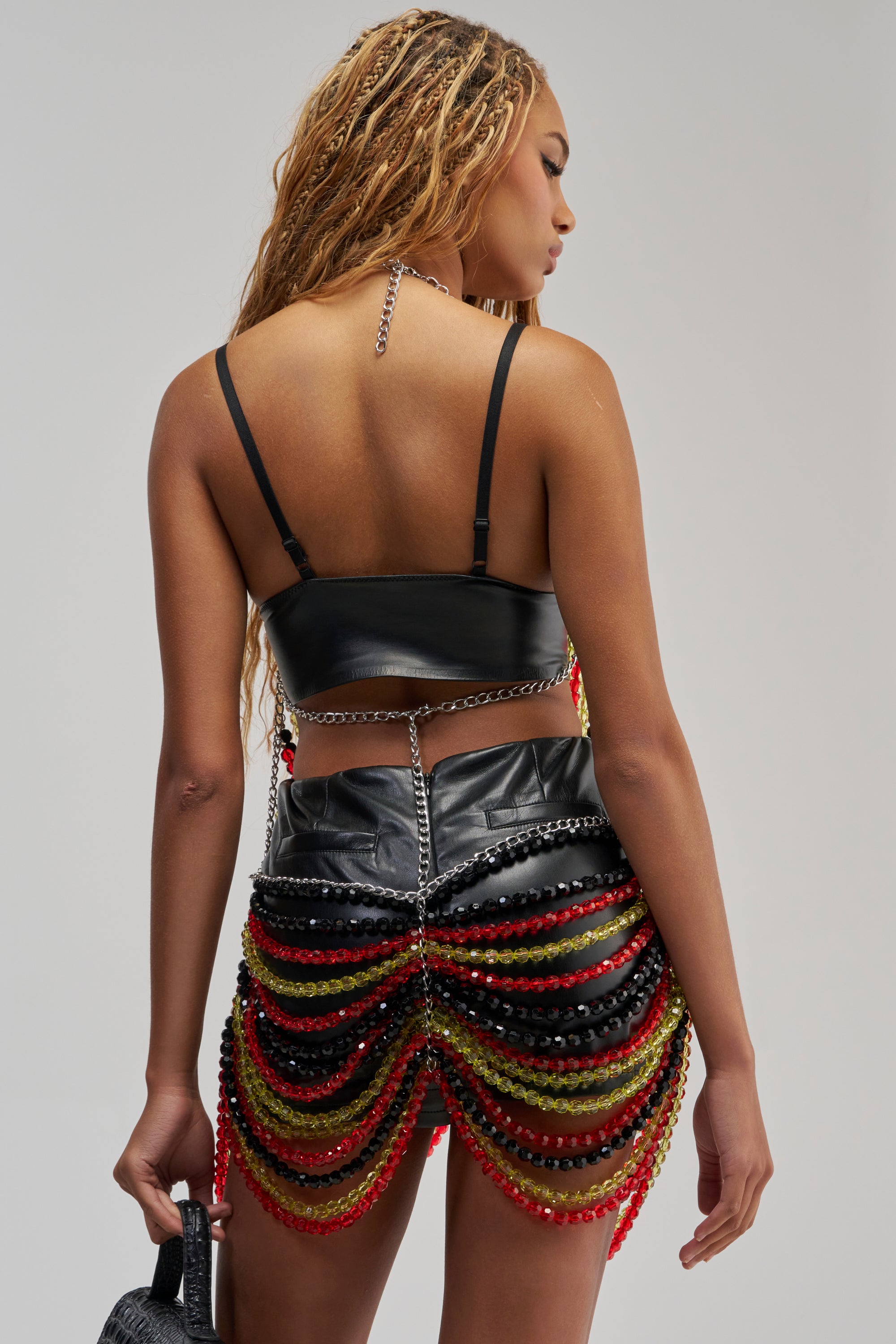 A woman with long braided hair faces away from the camera, wearing the striking CARNIVALE BEADED MINI DRESS IN GREEN MULTI—a vibrant choice perfect for festival styling or special occasions.
