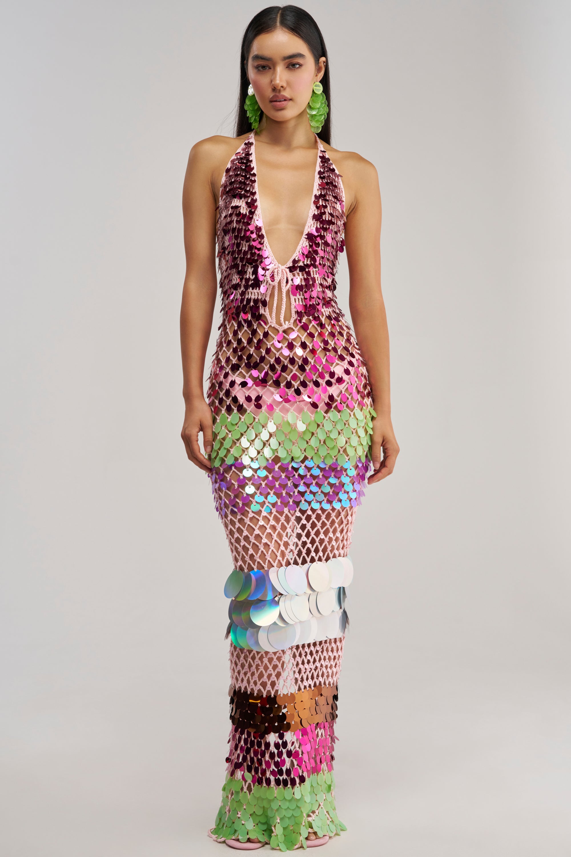 Wearing the PARTY CRASHER SEQUIN MAXI DRESS IN GREEN MULTI—a sleeveless, floor-length mesh gown embellished with bold, shiny sequins in pink, green, white, and silver—a woman poses against a plain light background, exuding glamorous vacation night style.