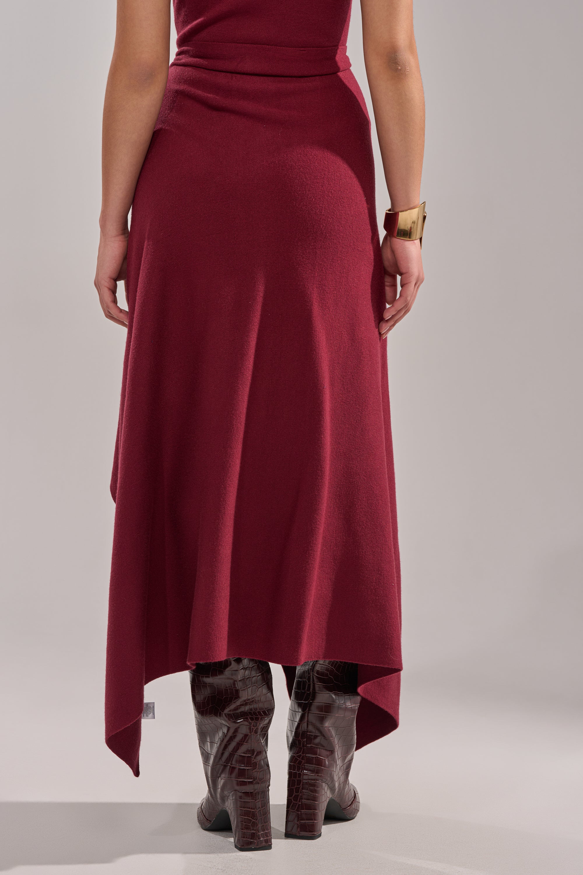 A person wearing the LOVER SWEATER MAXI SKIRT, styled with tall brown textured boots and a chunky gold bracelet, is shown from the back against a plain background. 5