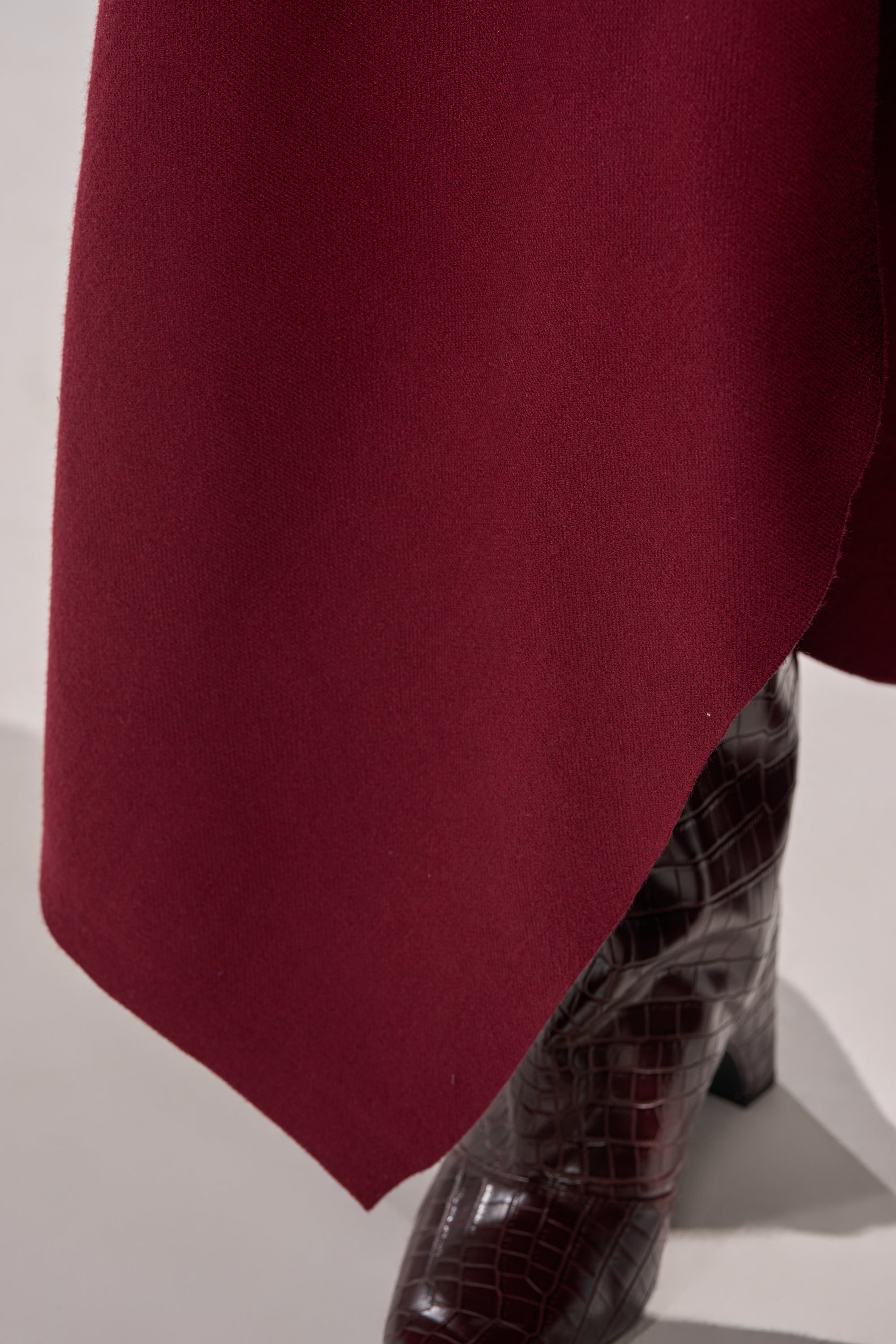 A close-up of the LOVER SWEATER MAXI SKIRT in wine-red draped over a leg, revealing a dark brown, crocodile-patterned leather boot underneath. 8