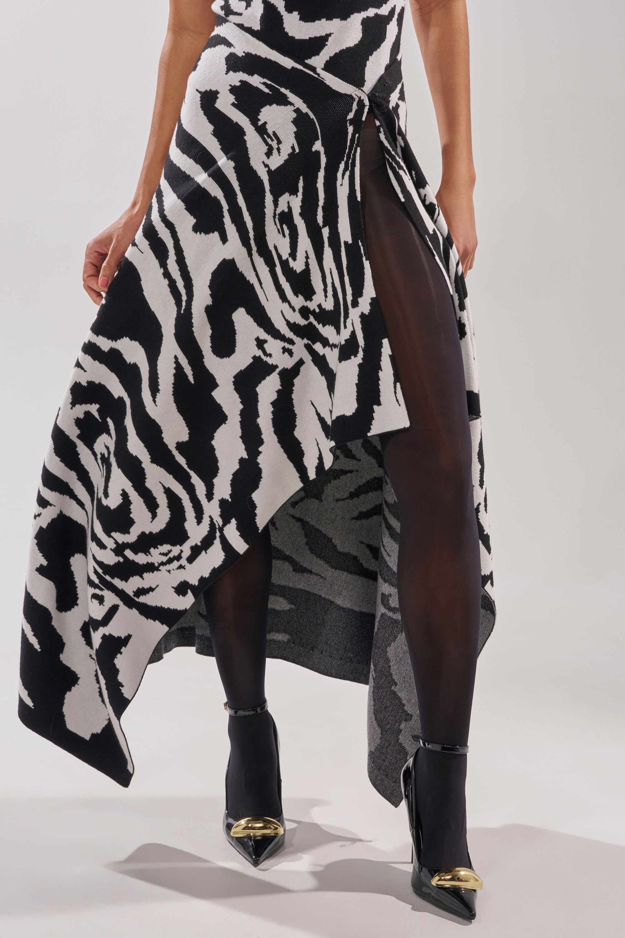 A person wearing the NATOMA FLORAL MAXI SKIRT, sheer black tights, and black high-heeled shoes with gold pointed toes stands against a plain background.