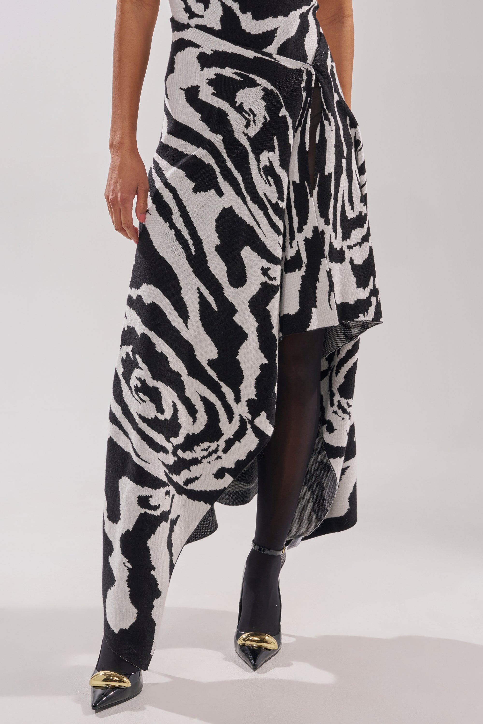 A person wears the NATOMA FLORAL MAXI SKIRT, styled with black tights and pointed heels with metallic gold tips, set against a plain light-colored background.