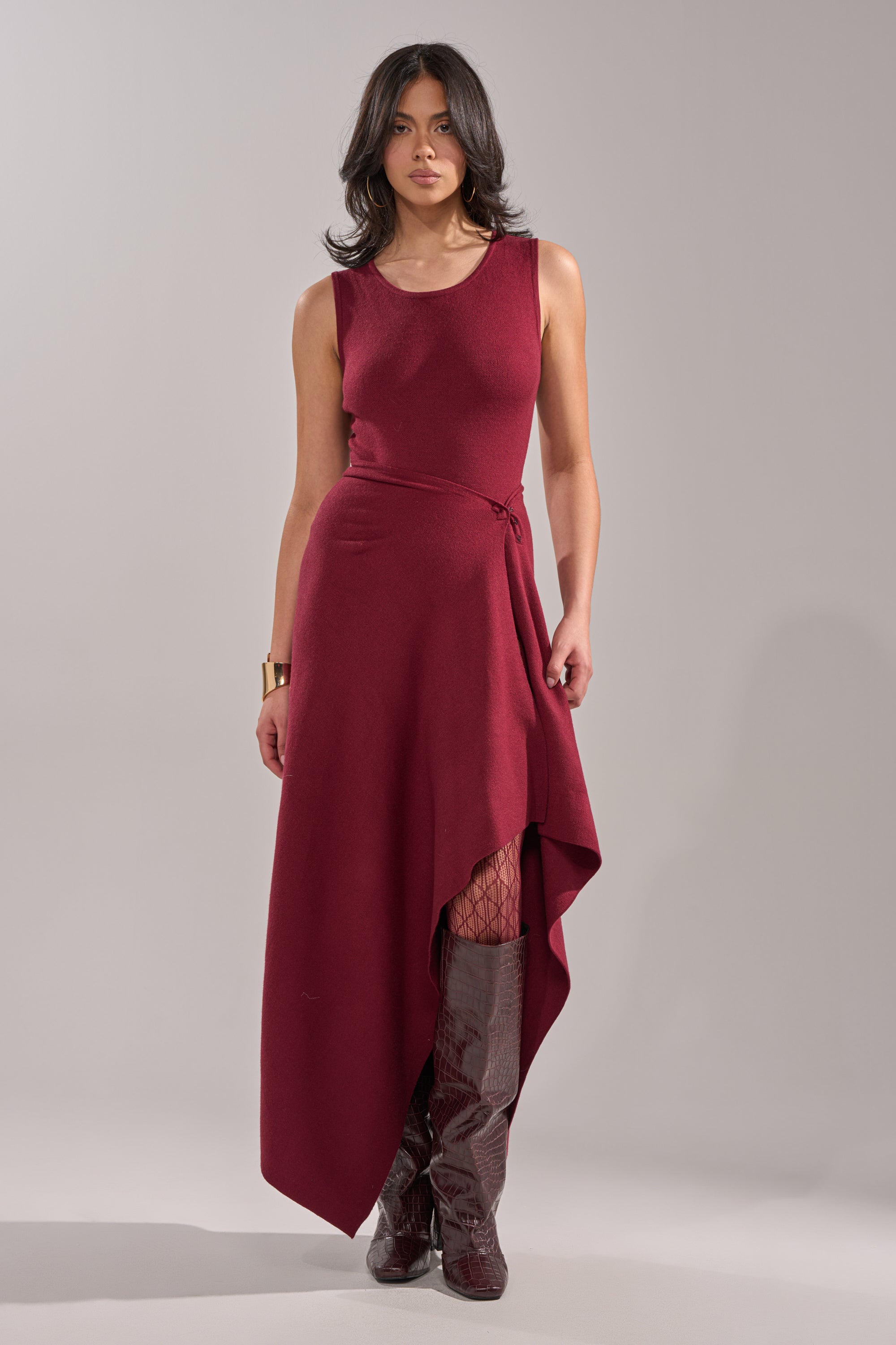 A woman with dark, wavy hair and a neutral expression wears the LOVER SWEATER BODYSUIT in burgundy, styled with patterned tights and knee-high burgundy boots against a plain background. 6