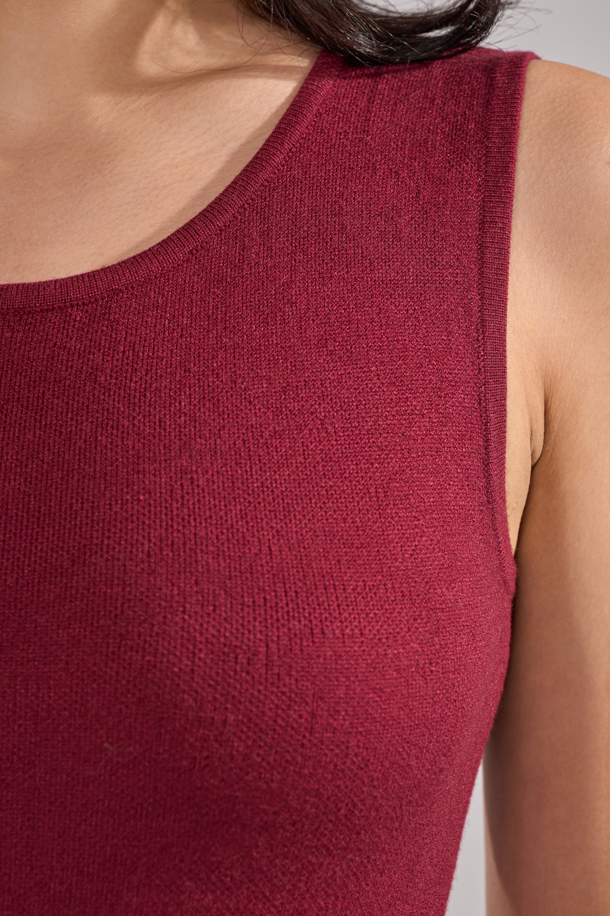 Close-up of a person wearing the LOVER SWEATER BODYSUIT in burgundy, featuring a scoop neckline and textured stretch-knit fabric. The sleeveless one-piece stands out against a neutral background, highlighting the shoulder and upper chest. 7