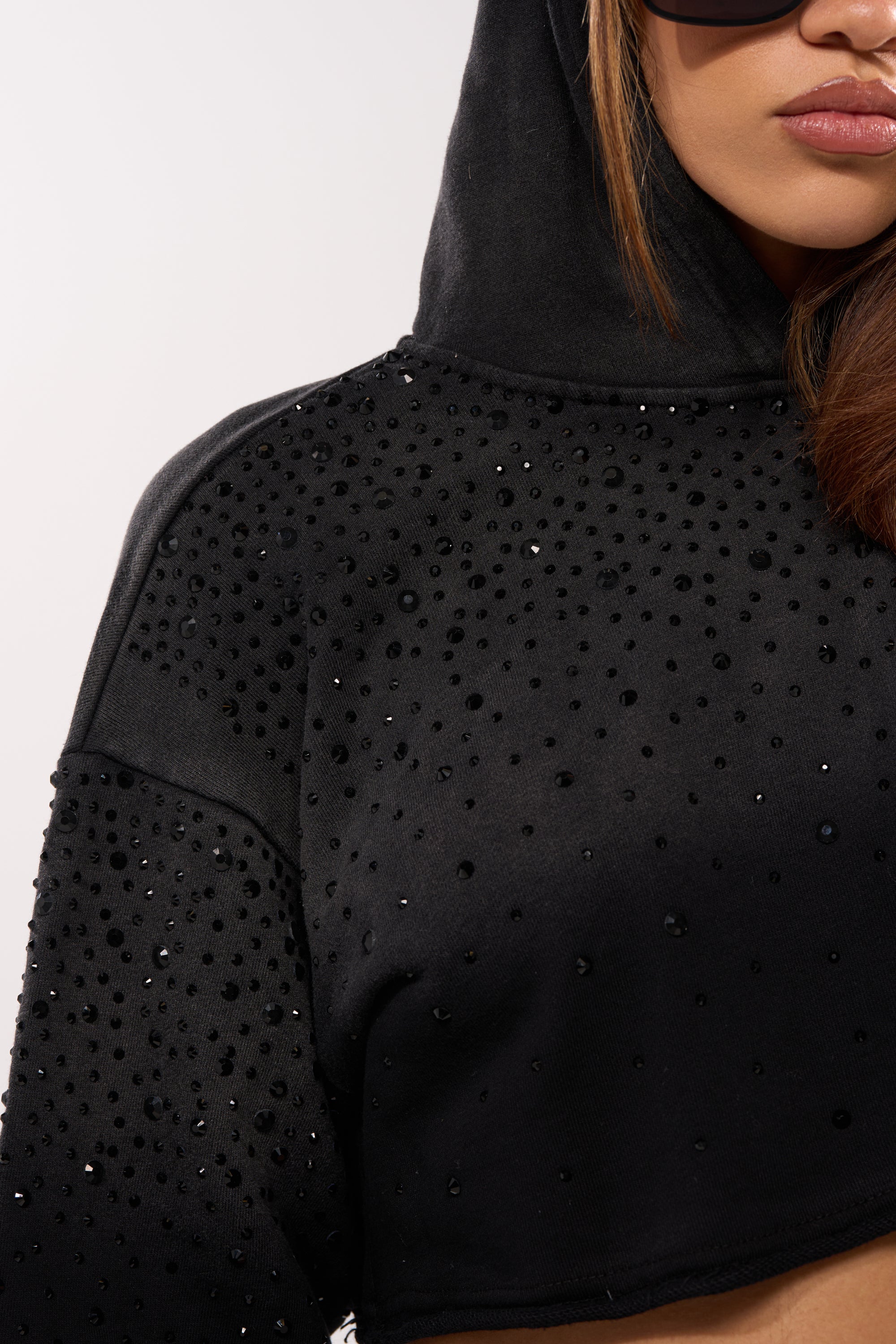 Close-up of a person in the SPARKLE AND SHINE MINERAL WASHED CROPPED HOODIE, featuring black rhinestones. The individual has long brown hair, sunglasses, and only the lower half of their face is shown. 7