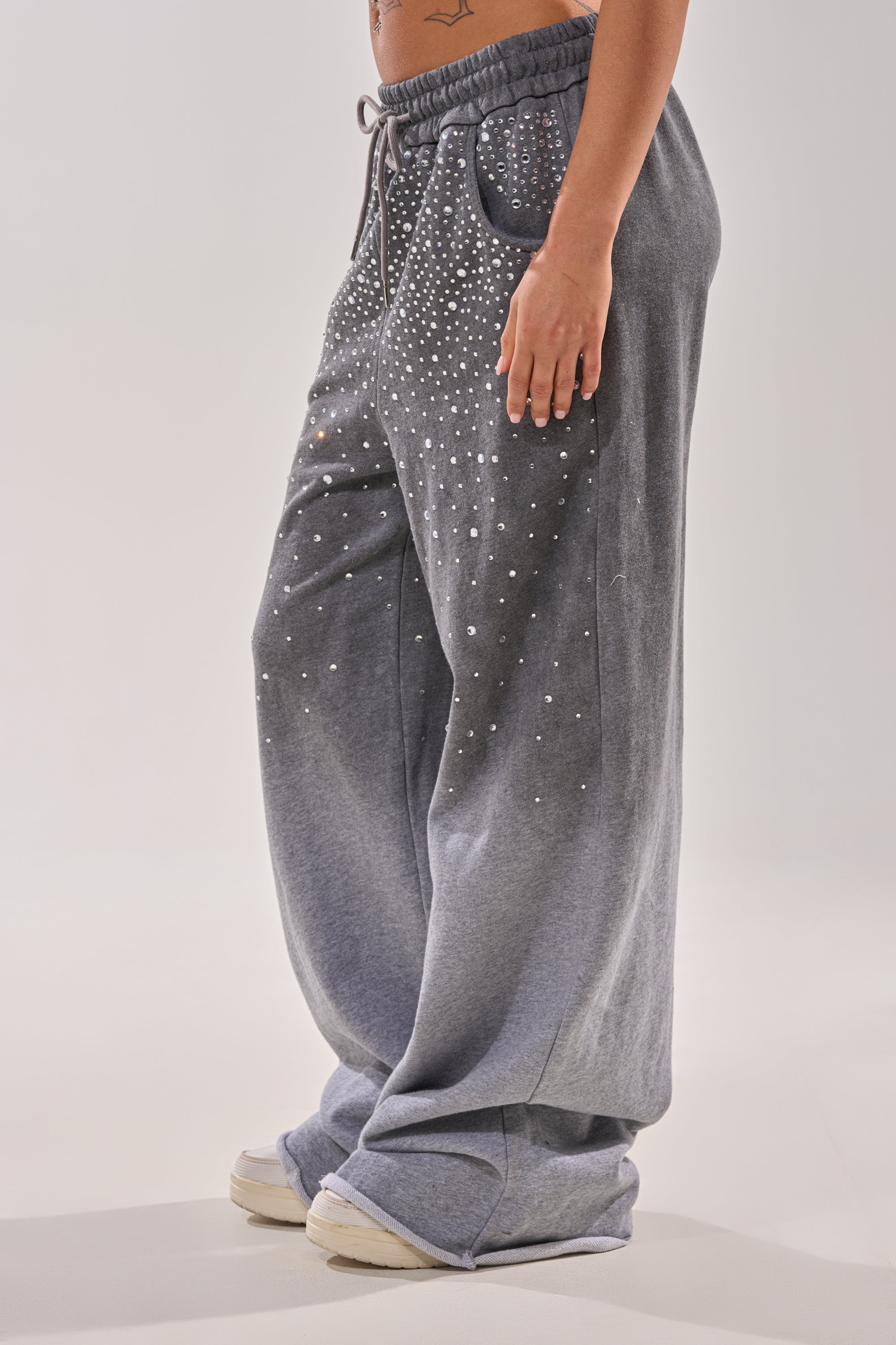 A person wearing the NIGHT SKY RHINESTONE JOGGER in a loose fit with sparkling embellishments and white sneakers. The image is cropped to show only the lower torso and legs. 3
