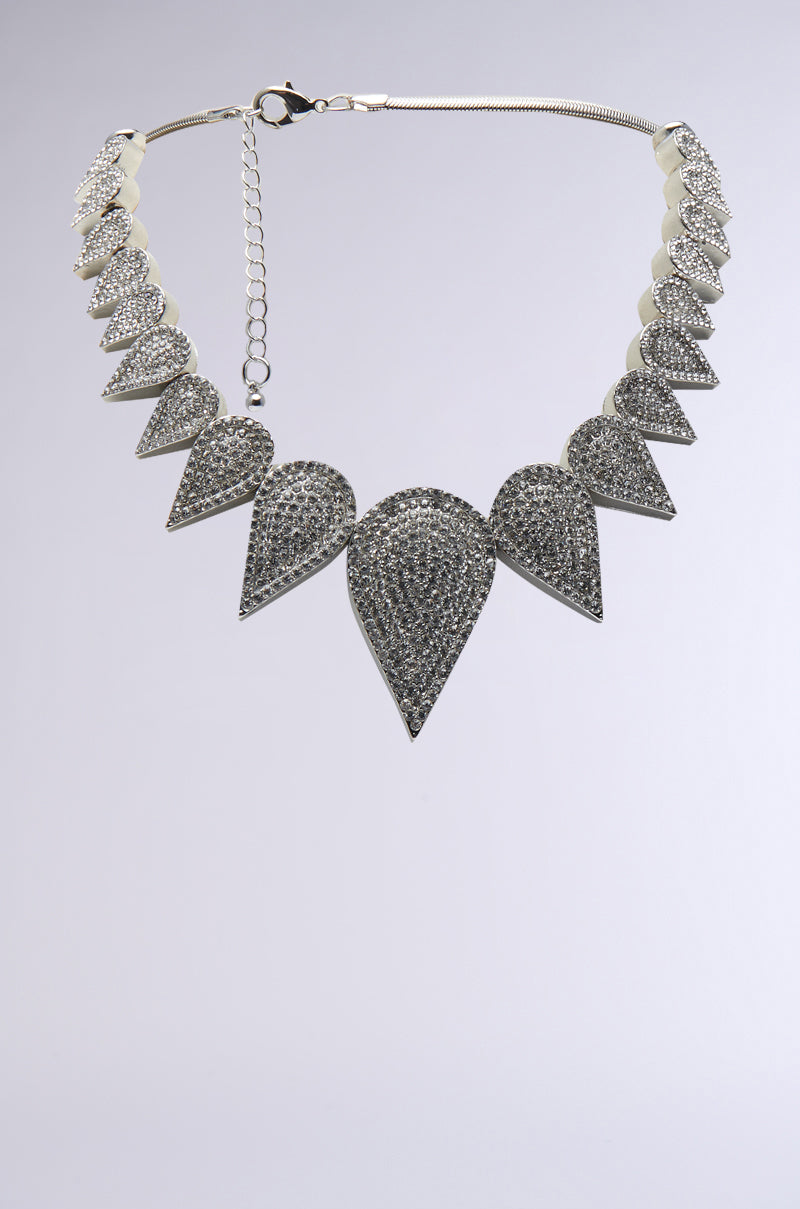 Introducing the ICE PRINCESS STATEMENT NECKLACE, featuring triangular gem-encrusted pendants arranged symmetrically. This silver piece is complemented by a sleek snake chain and adjustable clasp, creating a stunning contrast against the plain light gray background.