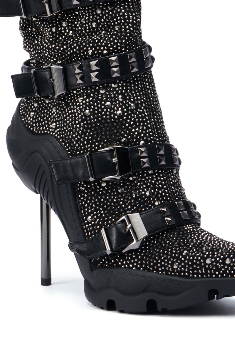 The AZALEA WANG EMBELLISHED BOOTIE IN BLACK showcases a sleek design with a pointed toe, embellished with dazzling rhinestones and decorative studs. This bootie is equipped with multiple adjustable straps featuring buckles and rests on a slender stiletto heel, offering a bold and stylish appearance.