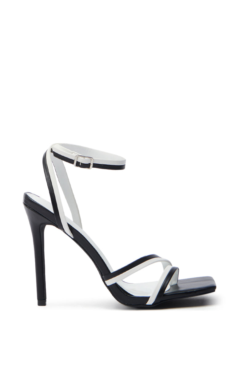 The AKIRA Nehara Black and White Stiletto Sandal, crafted from vegan leather, features a thin ankle strap with a buckle closure and slender crisscross straps. Its sleek design includes an open square toe and a pointed silhouette for a modern edge.