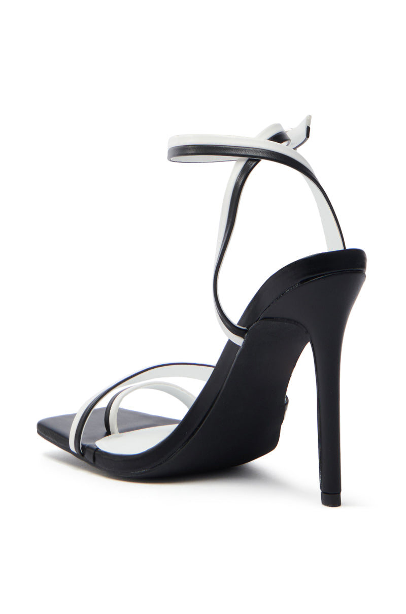 The AKIRA NEHARA Black and White Stiletto Sandal features a sleek black sole and heel, with thin black and white straps including an adjustable ankle strap. It has an open square toe design crafted from elegant vegan leather.