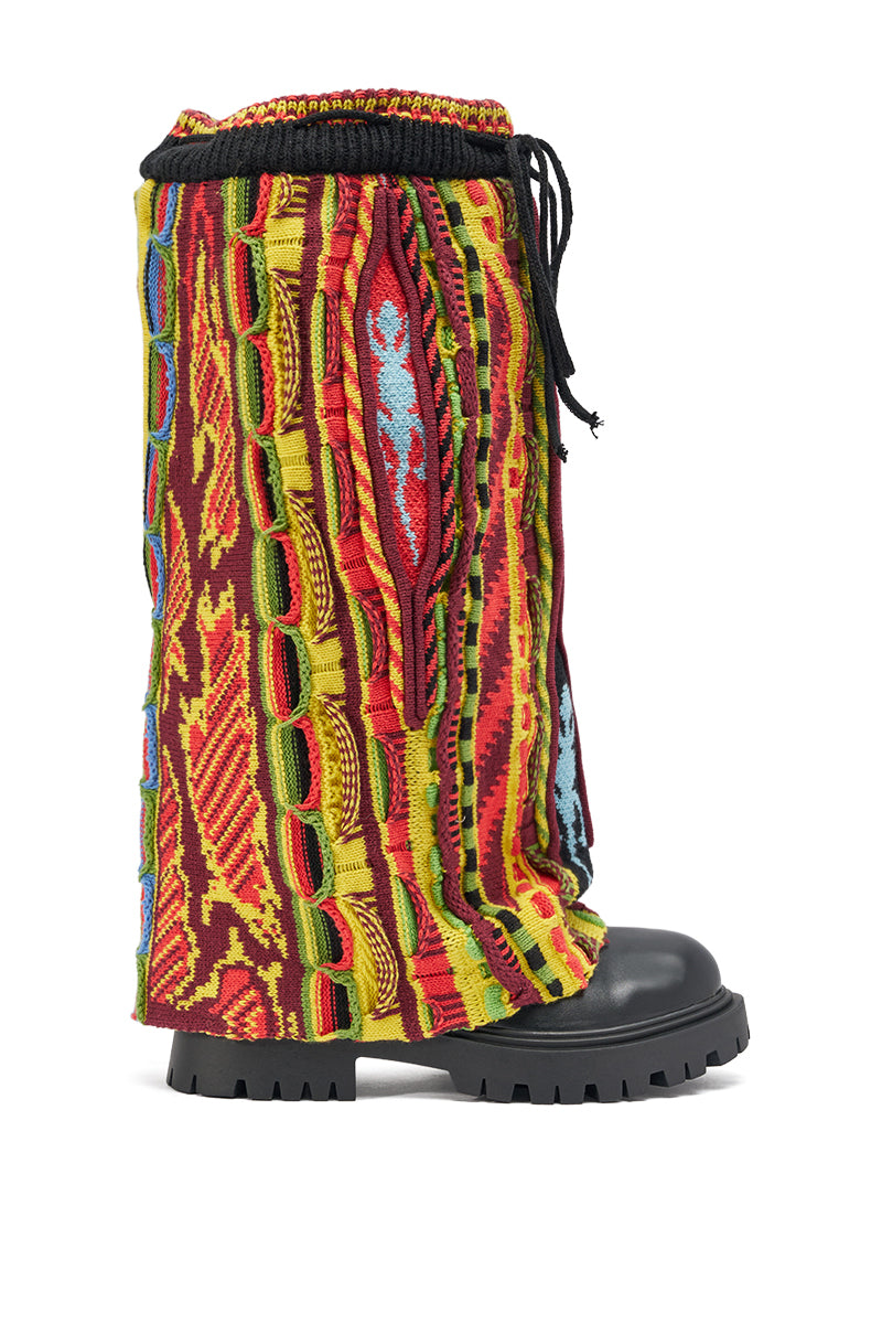 The AKIRA GOLD NEIL SWEATER COMBAT BOOTIE is a black chunky heel boot with colorful, textured multicolor knit leg warmers in vibrant red, yellow, green, blue, and orange patterns and features black laces at the top.