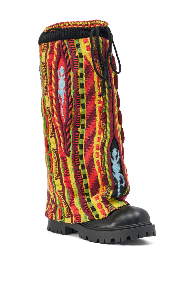 The AKIRA GOLD NEIL SWEATER COMBAT BOOTIE is a tall, multicolor knit boot with a chunky heel, thick black sole and toe, vibrant geometric red, yellow, blue, and black patterns, and black laces at the top.