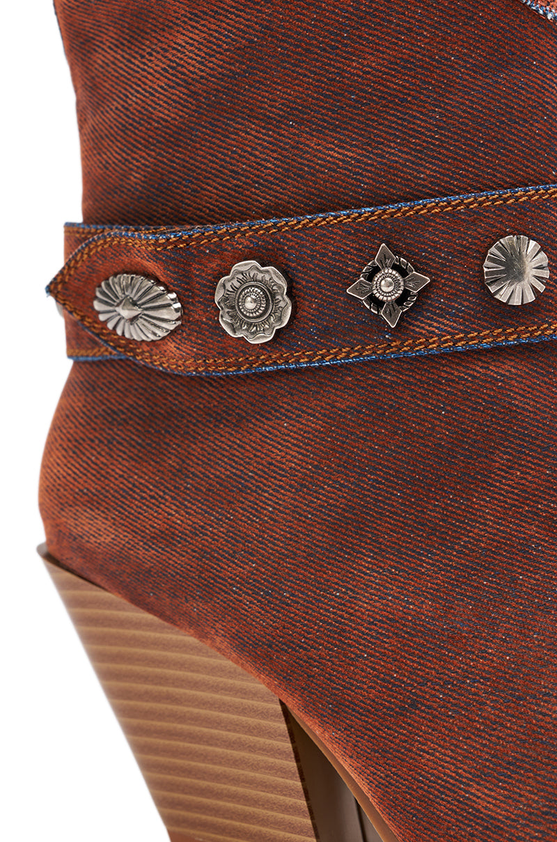 Close-up of the AZALEA WANG NEITH BURNT ORANGE DENIM WESTERN BOOTIE, featuring a decorative strap with silver flower and geometric studs and a stacked wooden heel for a classic chunky western bootie style.