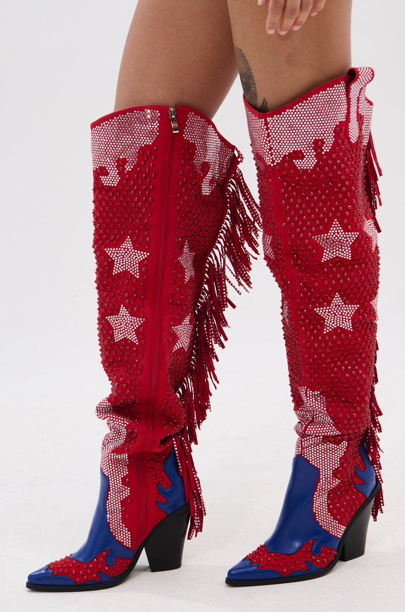 A woman wears the AZALEA WANG NELLA BLUE MULTI WESTERN EMBELLISHED BOOT—knee-high faux suede boots featuring white stars, fringe, blue toes and heels, plus stud and rhinestone accents. A thigh tattoo is slightly visible.