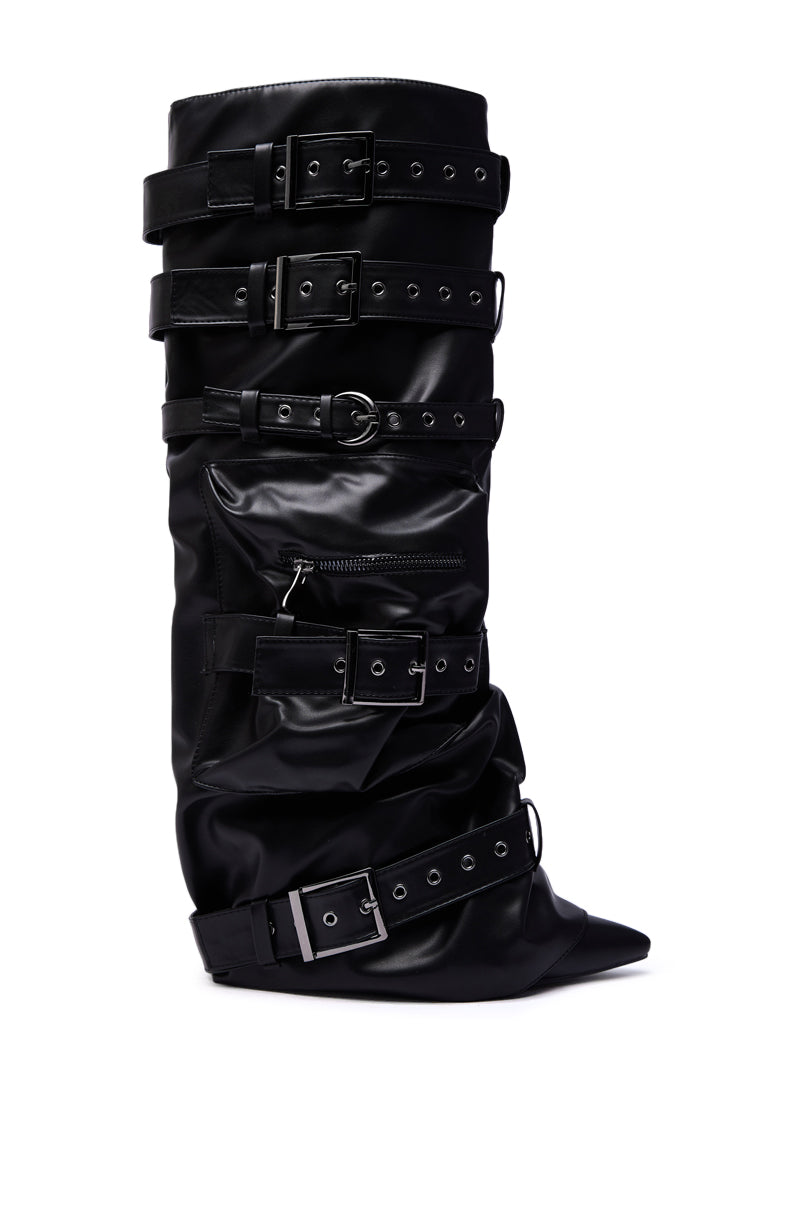 The AZALEA WANG NEMIANA BLACK BELT AND BUCKLES DETAIL BOOT is a black knee-high faux leather boot featuring a pointed toe, shiny finish, slouched design, silver buckles and straps, eyelets, and a side zipper pocket.