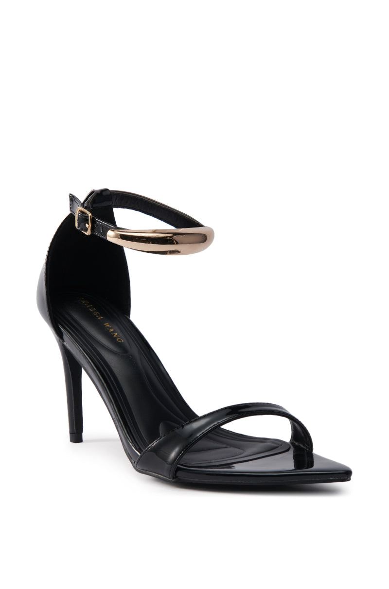 The AKIRA NEMTI BLACK STILETTO SANDAL features a black patent leather upper, slim toe strap, pointed toe, and adjustable ankle strap with gold buckle, shown against a white background.