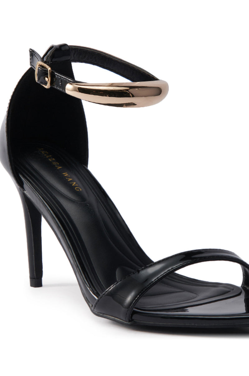 The AKIRA NEMTI BLACK STILETTO SANDAL features a glossy patent leather upper, thin toe strap, and an adjustable gold metallic buckle ankle strap, finished with a sleek stiletto heel for added elegance.