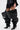 A person wears the AZALEA WANG NEMY BLACK KITTEN HEEL THIGH HIGH BOOT—an oversized, slouchy faux leather style with pointed toes—paired with a short ruffled black skirt and pleated black top.