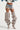 A stylish individual wearing a white crop top, denim shorts with faux fur trim, and the AZALEA WANG NEMY SNAKE EXTREME SLOUCH BOOT. The outfit is accessorized with a belt featuring multiple chains and metal charms. The person's face is not visible in the image.