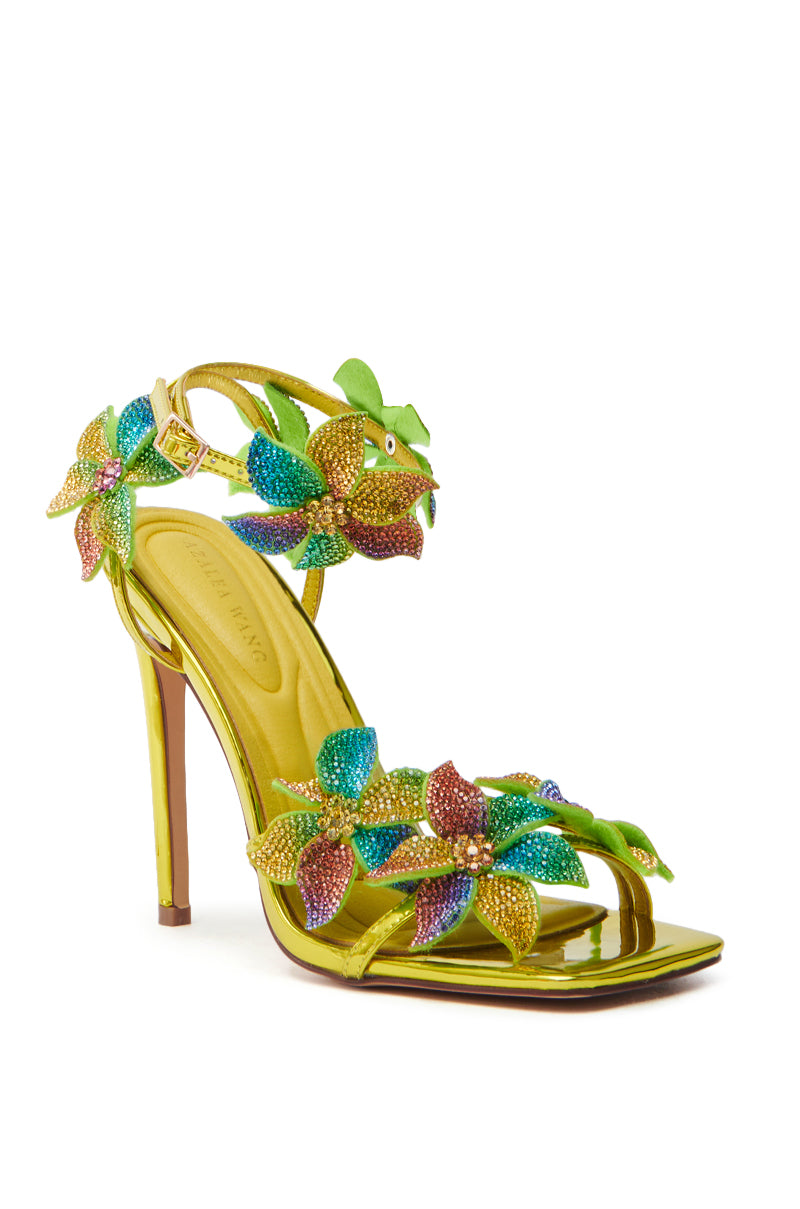 The AZALEA WANG NERIYA MULTI RHINESTONE FLOWER STILETTO SANDAL features a metallic gold finish with vibrant rhinestone flowers in green, purple, and orange hues. It boasts floral-embellished straps and a thin heel for an elegant touch.